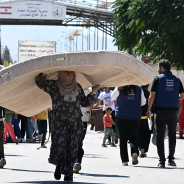 A woman carries a mattress over her head as she enters Syria from Lebanon via the Jusiyeh border crossing with Quseir in Syria's central Homs province on October 2, 2024.