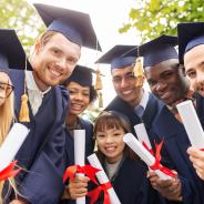 Smiling young graduates in gowns and mortarboards clutching diplomas
