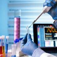Scientist holding tube and working with laptop at genetic lab 