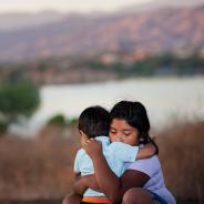 Brother and sister separated from parents are hugging each other in a foreign country, across a river. 