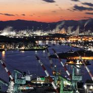 Night view of shipyard with tower cranes near the sea against chimney of oil refinery factory.