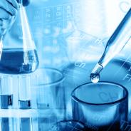 Hand of scientist holding flask with lab glassware and test tubes in chemical laboratory background.