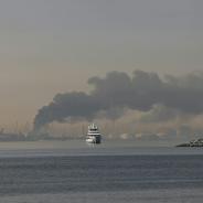A yacht sails past a plume of smoke rising from the port of Jebel Ali following a reported Iranian strike in Dubai on March 1, 2026.