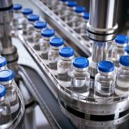 Closeup of ampules are being filled with vaccine and closed with blue caps.