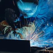 Industrial welder at work with sparks flying in shipyard setting.