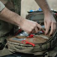  Military paramedic hands near open backpack with first aid kit, close up