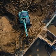  Excavator in Mining Quarry and Rock Crusher Facility on Sunny Day, Industrial mining site captured from above, featuring heavy machinery, material processing operations, rugged excavation terrain