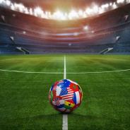 Green textured field in soccer stadium and soccer ball covered with multiple national flags symbolizing an international football tournament.