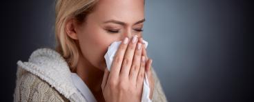 A woman sneezes into a tissue.