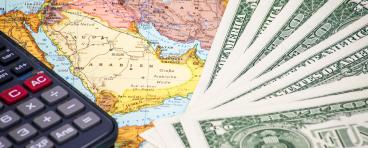 Money and a calculator rest on top of a map of the Middle East.