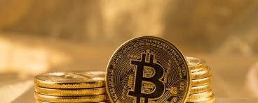 A Bitcoin leans against two stacks of Bitcoins.