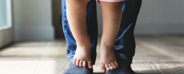A child stands on parent's feet.