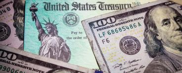 A stimulus check lies amongst hundred dollar bills.