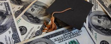 A graduation cap lies amongst $100 bills.