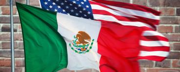 The Mexico and U.S. flags in front of a brick wall.