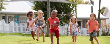 Five children run across a lawn.