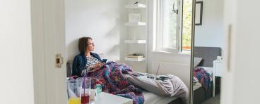 A woman lies in bed while looking out a window.