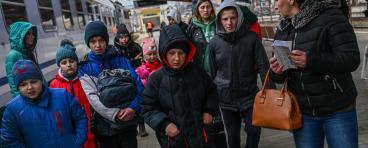 Ukrainian refugees walk down a street with their belongings.
