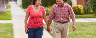 A Hispanic senior couple walks through a neighborhood.