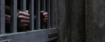 A prisoner grabs onto the bars of a jail cell.