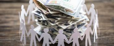 Paper cut-outs of people surrounding a pile of cash.