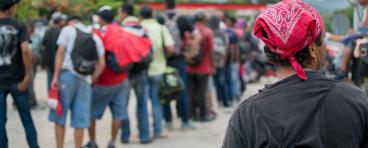 Line of Hispanic immigrants waiting outside with backs to viewer.
