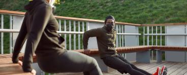 Two individuals in masks doing tricep exercises outdoors.