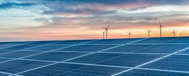 Solar panels with wind turbines in the distance at sundown.