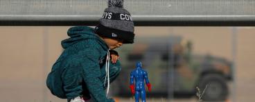 Child at border plays in the dirt with superhero toy