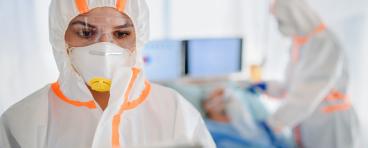 Healthcare workers wear hooded coveralls and masks while interacting with patients.
