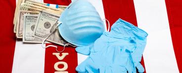 A mask, gloves, money, and letters spelling "vote" lie on a flag of the United States.