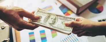 Close up of hands and business giving as illustrated by the exchange of US currency
