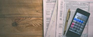 tax forms on table with calculator and pen on top