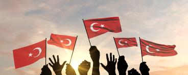 Turkish flags held up by hands against the sky