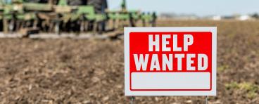 "Help wanted" sign superimposed on plowed land