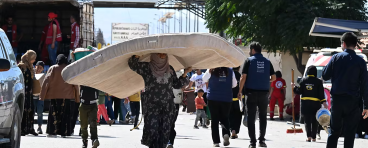 A woman carries a mattress over her head as she enters Syria from Lebanon via the Jusiyeh border crossing with Quseir in Syria's central Homs province on October 2, 2024.