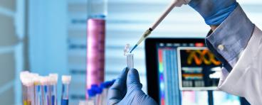 Scientist holding tube and working with laptop at genetic lab 