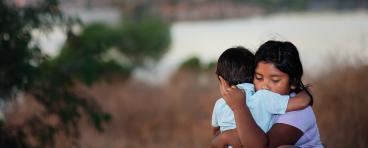 Brother and sister separated from parents are hugging each other in a foreign country, across a river. 