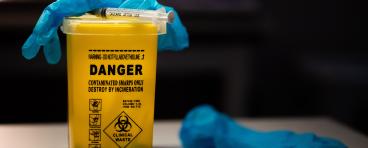 Gloves and syringe on top of sharps container