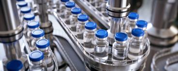 Closeup of ampules are being filled with vaccine and closed with blue caps.