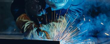 Industrial welder at work with sparks flying in shipyard setting.