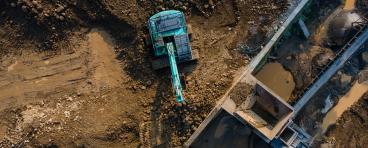  Excavator in Mining Quarry and Rock Crusher Facility on Sunny Day, Industrial mining site captured from above, featuring heavy machinery, material processing operations, rugged excavation terrain