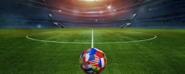 Green textured field in soccer stadium and soccer ball covered with multiple national flags symbolizing an international football tournament.
