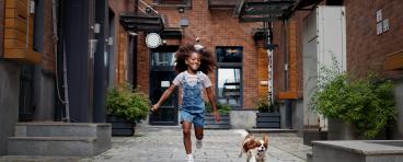 Child running alongside dog in city environment